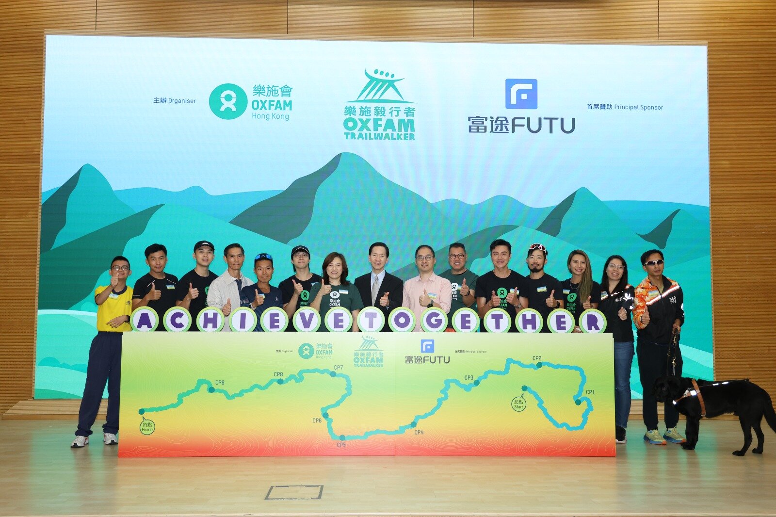 樂施毅行者2025的活動主題為「同毅同行 不懈信念」，眾嘉賓一同主持啟動儀式，為活動揭開序幕。左起：匡智獅子會晨崗學校蔡垂希同學、匡智獅子會晨崗學校施性概老師、星級毅行者伍富橋、毅行教室慈善基金創辦人陳國強、精英毅行者楊志成、樂施毅行者活動大使吳業坤、樂施會總裁潘寶屏、樂施毅行者督導小組召集人陳智思、富途證券國際（香港）有限公司董事總經理謝志堅、樂施會籌募及傳訊總監王灝鳴、樂施毅行者宣傳大使黃浩然、星級健身教練黃家灝、星級運動員鄭麗莎、香港傷健共融網絡經理(運動康復及籌款)林旭蕾、視障跑手陳智順及導盲犬Ronny。